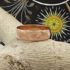Front view of plain domed copper ring resting on a light-colored tree branch with a black and earth tone graphic in the background.