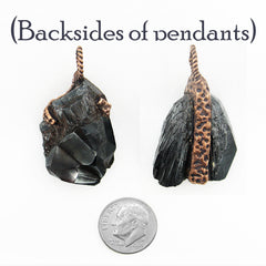 Two hematite crystal pendants showing their back sides with copper wire wrapping, displayed next to a US quarter for scale on a white background with the text '(Backs of pendants)' at the top.