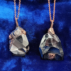 Two raw crystal pendant necklaces with copper chains and hematite crystal pendants, displayed on a vibrant blue velvet fabric background.