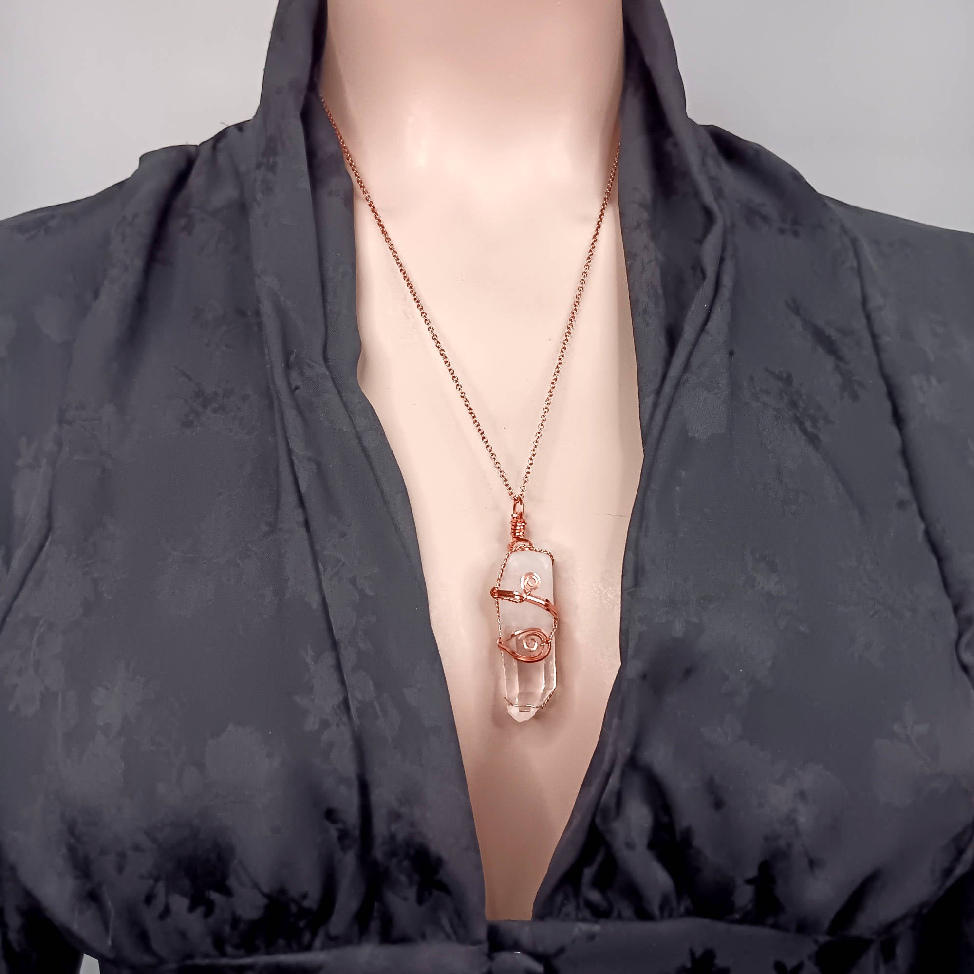 Model wearing a dark floral-patterned garment with a necklace featuring a clear crystal wire wrapped copper quartz pendant.