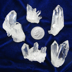 View of 5 different clear quartz crystal clusters next to a dime to show scale on a dark background