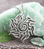 Tribal Sun Spiral Pendant Necklace Wiccan Pagan Witchy Mystical Alternative Gothic Goth Occult Jewelry Fine Silver with chain in front of rough green rock